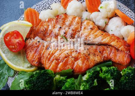Lachssteak mit Gemüse Blumenkohl, Brokkoli, Karotten und grünen Bohnen. Salat aus Rucola und Gemüse mit Lachs. Nahaufnahme. Stockfoto