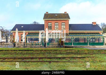 As, Limburg, Belgien. Dezember 2023. Fassade des Restaurants Asch im Gebäude des alten Bahnhofs, Terrasse mit Stühlen und Tischen, stillgelegte Gleise Stockfoto