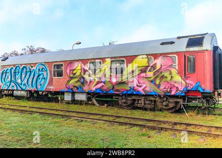 As, Limburg, Belgien. Dezember 2023. Stillgelegte Bahngleise des alten Bahnhofs mit einem sehr alten roten Pkw mit Türen und Fenstern, die mit bemalt waren Stockfoto