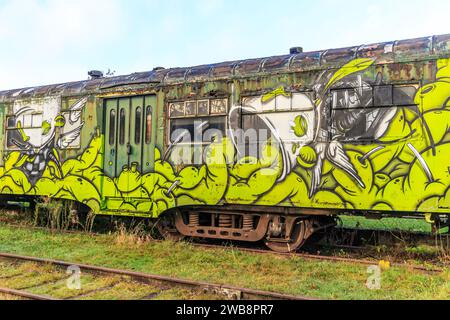 As, Limburg, Belgien. Dezember 2023. Alter beschädigter PKW mit grün lackierten Türen und Fenstern, stillgelegte Bahngleise des alten Bahnhofs, Abblätterung Stockfoto