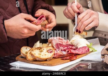 Ein paar Touristen essen verschiedene Wurstwaren, darunter Schinken, Salami und coppa, zusammen mit frischem Mozzarella, Käsescheiben und rustikalem Brot Stockfoto