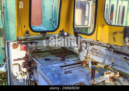 Innenraum eines sehr alten, zerlegten Eisenbahncockpits, Steuerhebel, Metall korrodiert und verrostet durch die Zeit, Fenster, grüner Pkw im Hintergrund Stockfoto