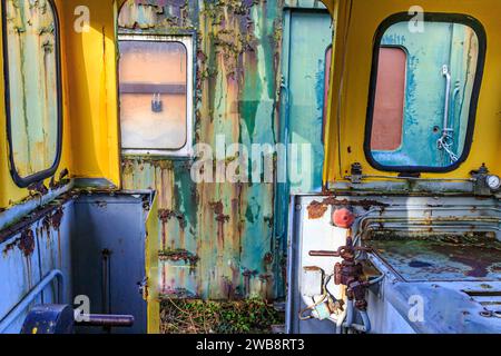 Innenraum des sehr alten Eisenbahncockpits ohne Türen, Metallwände korrodiert, abblättert und rostig von der Zeit eines Personenkraftwagens im Hintergrund Stockfoto