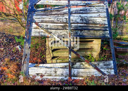 Tür oder Wand aus Holzdielen eines kaputten Eisenbahnwagens mit rostigem Metallrahmen, der auf Betonschwellen inmitten wilder Vegetation ruht, Hinterhof einer alten Stilllegung Stockfoto