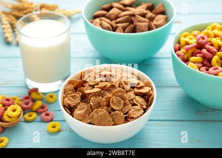 Auswahl an Müsli in blauen Schüsseln, schnelles Frühstück und Milch auf blauem Holzhintergrund. Draufsicht Stockfoto