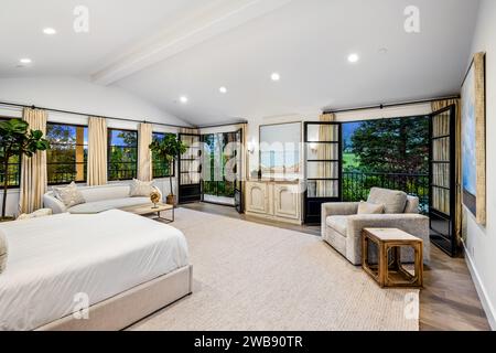 Ein elegant eingerichtetes Hauptschlafzimmer mit einem großen Himmelbett, einer hohen Decke und Glastüren, die einen Blick auf den Hinterhof bieten Stockfoto