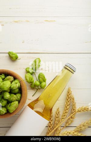 Bierflasche mit Hopfen und Weizen auf weißem Hintergrund, Nahaufnahme. Draufsicht Stockfoto