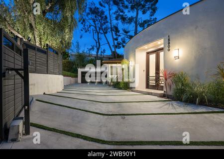 Ein malerischer Hinterhof mit einem Steingang und Stufen, die zu einem Vordereingang führen, mit üppigem Gras und Bäumen im Hintergrund Stockfoto