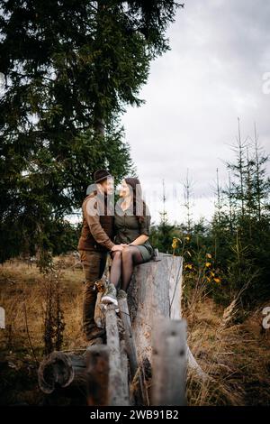 Ein junges, nettes Paar, der Jäger und seine Dame, sehen sich an und sitzen zusammen auf einem Zaun in der Natur Stockfoto