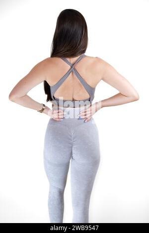 Eine junge Frau mit langen schwarzen Haaren, die Aktivkleidung trägt, die Hände auf den Hüften in einer Yoga-Pose steht Stockfoto