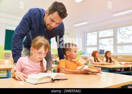 Männlicher Lehrer, der weiblichen Schülerin beim Lesen von Büchern hilft, während sie im Klassenzimmer auf der Bank sitzt Stockfoto