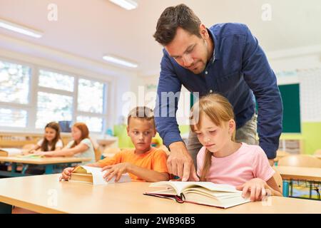 Männlicher Lehrer hilft dem Schüler beim Lesen von Büchern auf der Bank im Klassenzimmer Stockfoto