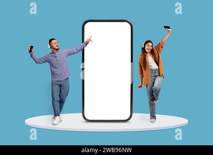 Fröhliches Duo mit Gadgets neben dem großen Telefonbildschirm Stockfoto