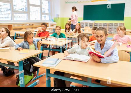 Lächelnder Grundlehrer liest dem Schulmädchen im Klassenzimmer ein Buch Stockfoto