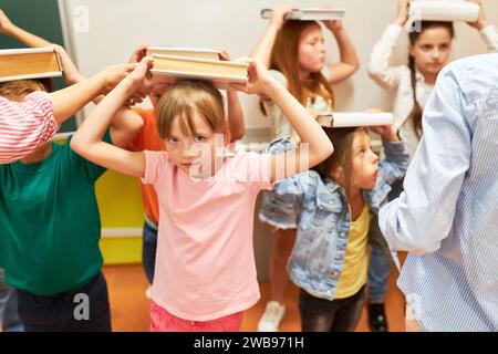 Porträt des Schulmädchens, das Buch auf dem Kopf mit Klassenkameraden während der Aktivität im Unterricht balanciert Stockfoto