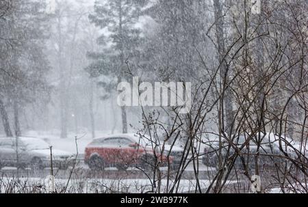 Schneebedeckte Stadtstraße bei starkem Schneefall. Auf dem Bürgersteig gibt es viel Schnee, Autos und Äste. Stockfoto