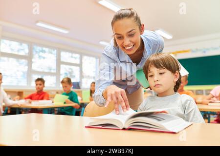 Grundschullehrerin, die Schülerin beim Lesen von Büchern im Klassenzimmer unterstützt Stockfoto