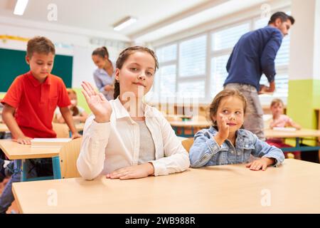 Porträt eines Schulmädchens, das mit einer Freundin winkt, die im Klassenzimmer auf einer Bank sitzt Stockfoto