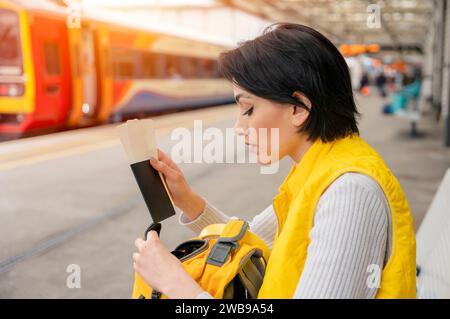 Junge Frau mit Pass und Fahrkarten, die am Bahnhof auf den Zug wartet und das Reisekonzept genießt Stockfoto