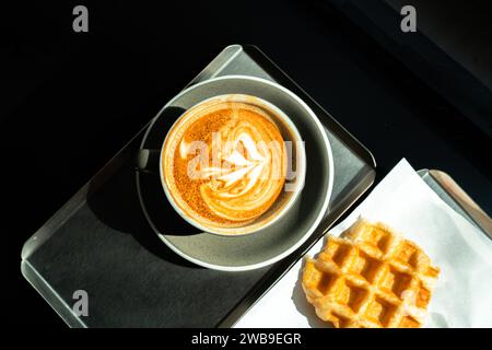 Späte Kaffeekunst auf dem Holztisch. Entspannungskonzept. Eiskaffee Latte mit weichem, weißem Milchschaum und durchscheinendem Sonnenlicht. Foto eines Bechers Stockfoto