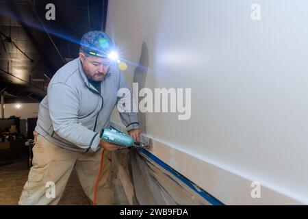 Der Auftragnehmer nagelt Holzverkleidungen während der Installation in einem neuen Haus mit einer Druckluftpistole Stockfoto