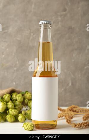 Bierflasche mit Hopfen und Weizen auf grauem Hintergrund, Nahaufnahme. Draufsicht Stockfoto