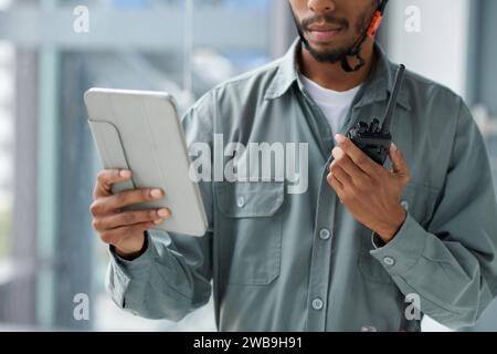 Zugeschnittenes Bild des Vorarbeiters, der das Dokument auf einem Tablet-Computer überprüft und über Walkie-Talkie kommuniziert Stockfoto