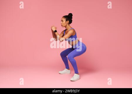 Entschlossene, Sportliche Junge Schwarze Dame, Die Tief Im Squat Trainieren, Studio Stockfoto
