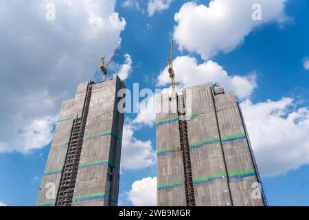 Zwei stehende Hochhäuser im Gerüst sind mit technischem Gewebe bedeckt, mit einer Schutzplane mit Kränen auf der Oberseite, gegen den Rücken Stockfoto