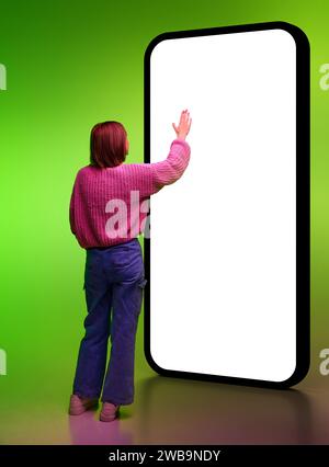 Volle Länge der jungen Frau, die den Bildschirm eines riesigen Smartphones im Neonlicht berührt. Mockup für neue mobile Apps oder Websites. Stockfoto