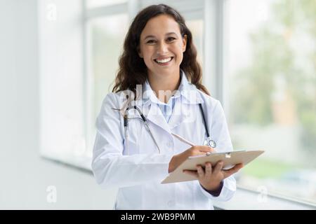 Positive junge Ärztin macht Notizen in Zwischenablage Stockfoto