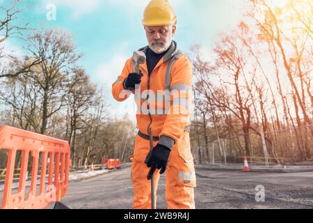 Bauarbeiter, der die Straße niederschlägt und bei Bauarbeiten Stahlstifte mit einem Klumpenhammer ausräumt. Der Baumeister hämmert während der Straßenfahrt Stahlstäbe in den Asphalt Stockfoto