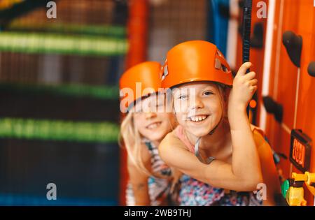 Zwei glückliche Schulmädchen in Sporthelmen im Kletterkurs. Indoor Boulderkurs für Schulkinder. Kinder genießen den Vergnügungspark Stockfoto