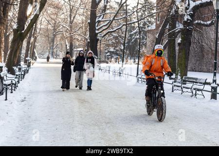 Krakau, Polen, 9. Januar 2024. Ein Liefermann fährt mit dem Fahrrad auf dem Wahrzeichen Planty Park, um im Zentrum der Stadt Essen zu liefern, da die Temperaturen deutlich unter Null fielen und der Schnee den größten Teil der Stadt bedeckt. Quelle: Dominika Zarzycka/Alamy Live News. Stockfoto