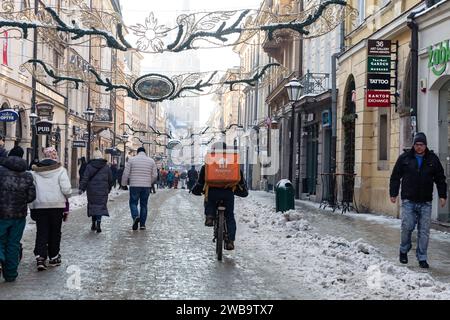 Krakau, Polen, 9. Januar 2024. Ein Liefermann fährt mit dem Fahrrad auf der berühmten Florianska Straße, um Lebensmittel im Zentrum der Stadt zu liefern, da die Temperaturen deutlich unter Null fielen und der Schnee den größten Teil der Stadt bedeckt. Quelle: Dominika Zarzycka/Alamy Live News. Stockfoto