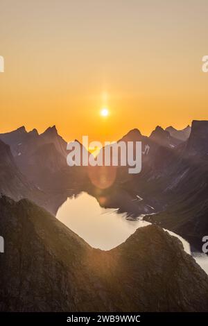 Der vertikale Rahmen fängt die Mitternachtssonne ein, die einen warmen Glanz über Reinebringens scharfen Gipfeln im norwegischen Lofoten ausstrahlt, während die Reflexion der Sonne schimmert Stockfoto