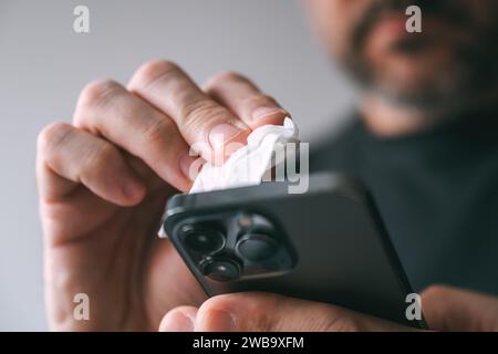 Mann reinigt Mobiltelefongerät mit nassem Wischtuch, selektiver Fokus Stockfoto