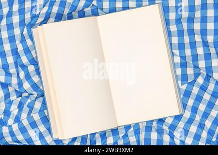 Öffnen Sie Buchseiten auf kariertem Tuch, Draufsicht Stockfoto