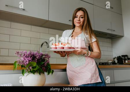 Die Herstellung von roten Samt-Cupcakes. Frau Hand, die Zuckerstreusel auf Cupcake. Stockfoto