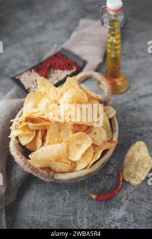 Herzhafte Chips in einer handgefertigten Kraftschale auf grauem Hintergrund. Kartoffelchips mit Gewürzen und Paprika verschiedener Art. Stockfoto