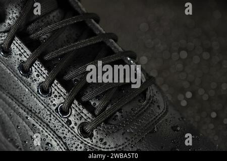 Neue wasserdichte Winterstiefel aus Leder mit Wassertropfen auf schwarzem Hintergrund in Nahaufnahme. Schuhkonzept. Stockfoto