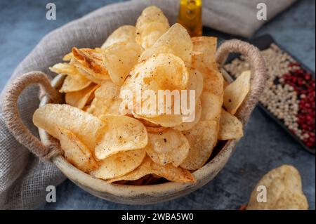 Herzhafte Chips in einer handgefertigten Kraftschale auf grauem Hintergrund. Kartoffelchips mit Gewürzen und Paprika verschiedener Art. Nahaufnahme Stockfoto