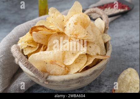 Herzhafte Chips in einer handgefertigten Kraftschale auf grauem Hintergrund. Kartoffelchips mit Gewürzen und Paprika verschiedener Art. Stockfoto