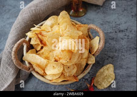 Herzhafte Chips in einer handgefertigten Kraftschale auf grauem Hintergrund. Kartoffelchips mit Gewürzen und Paprika verschiedener Art. Nahaufnahme, Draufsicht Stockfoto