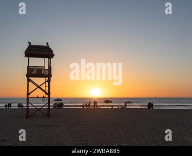 Menschen beobachten den Sonnenuntergang am Strand in der Nähe des Wachturms von Rettungsschwimmer in Agadir, Marokko, Nordafrika Stockfoto