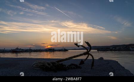 Ein alter rostiger Anker mit einem Seil liegt am Rand eines Piers in einer Bucht mit Fischerbooten in Skioni, Griechenland Stockfoto