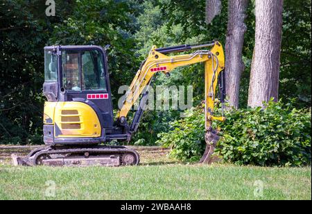 Ein kleiner gelber Traktor mit Schaufel und Raupenketten im Park in der Nähe eines Baumes Stockfoto