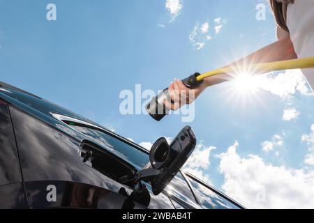 Frau, die eine Kappe für die Ladestation für Elektroautos öffnet und ein Ladegerät einsteckt Stockfoto