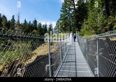 Eine Frau überquert eine Hängebrücke im Wald des Elk Falls Park in der Nähe des Campbell River, British Columbia, Kanada Stockfoto