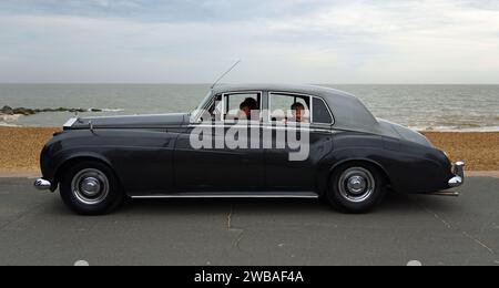 Vintage Rolls Royce Motor Car parkte an der Strandpromenade Strand und Meer im Hintergrund kleine Jungen, die aus Fenstern heraus. Stockfoto